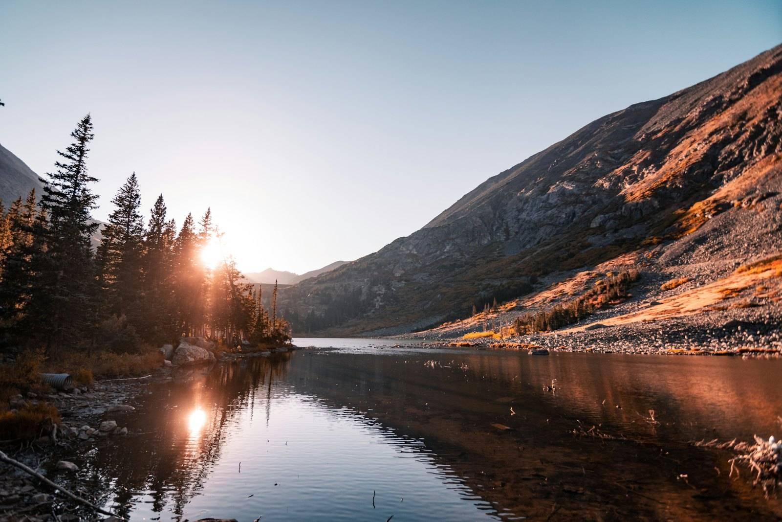 The sun shines on a mountain lake surrounded by pine trees
