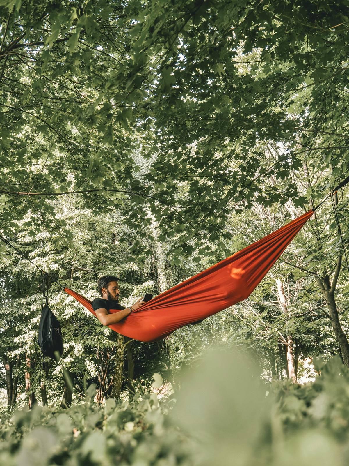 Man on red hammock surrounded by trees during daytime