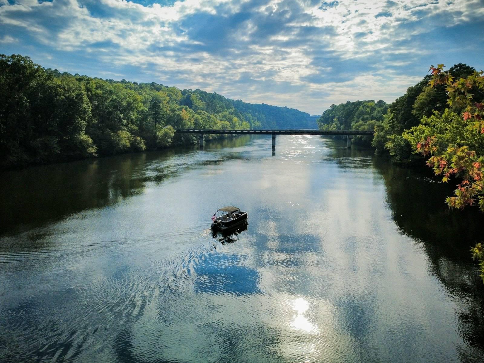 Boat on a wide river with forested banks and bridge