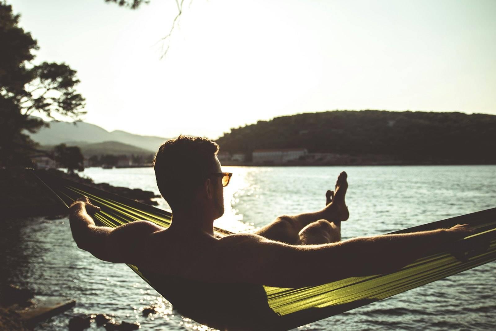 Silhouette of woman sitting on hammock by the sea during daytime